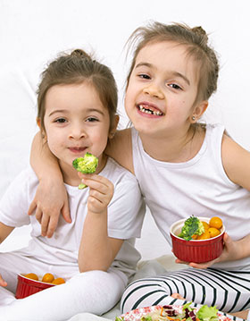 Two young sisters eating vegetables.