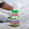 A bottle of 21st Century VitaJoy Melatonin 10 mg Extra Strength gummies on a bed with a woman sleeping in the background.