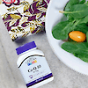 A bottle of 21st Century Co Q-10 30 mg capsules laying on a table next to a dinner plate of salad and napkin.