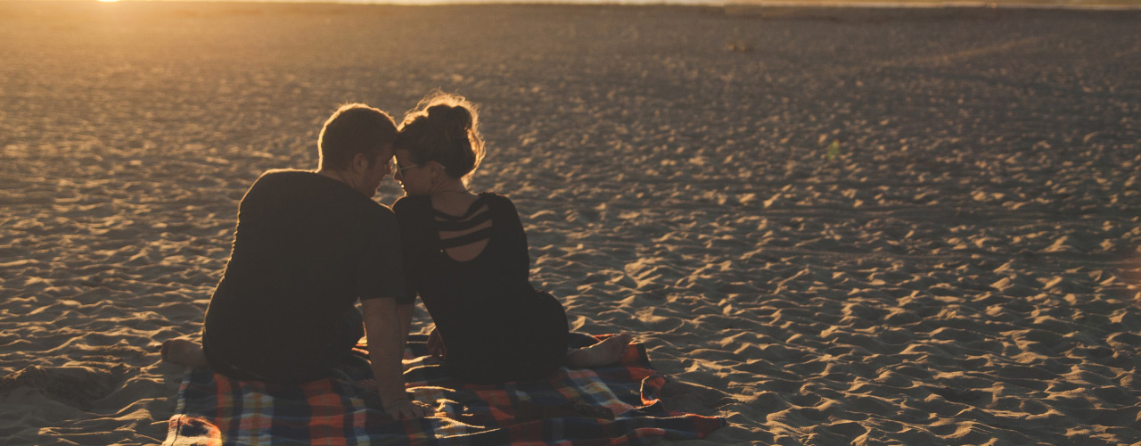 A couple snuggling on the beach watching the sunset.