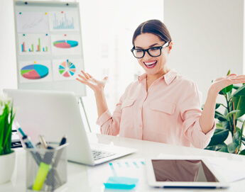 A girl sitting at her office desk smiling and looking happy while working.