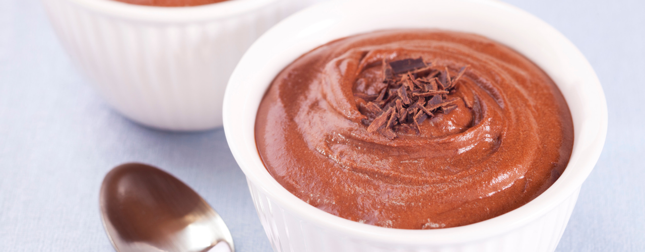 A chocolate dessert in a white cup a spoon next to it.