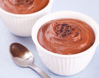 A chocolate dessert in a white cup a spoon next to it.