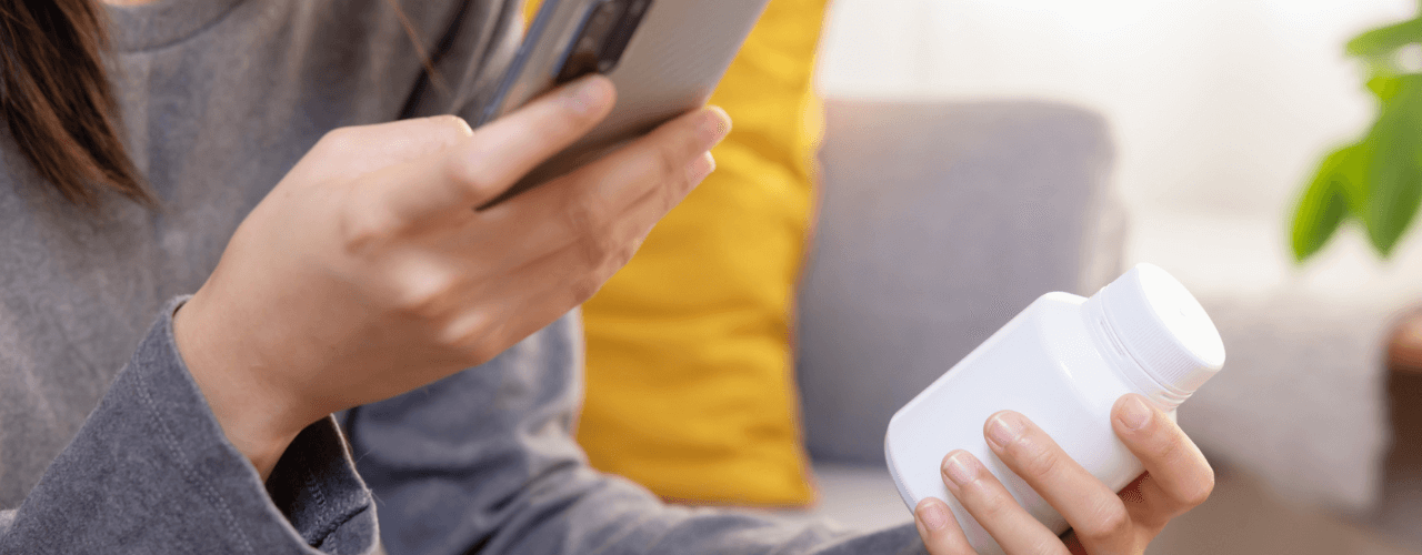 girl holding vitamin bottle and looking at phone