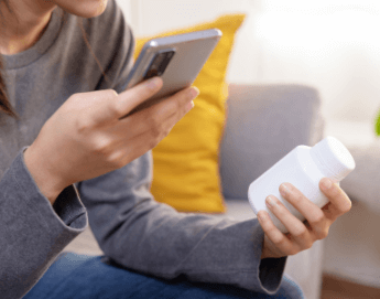 girl holding vitamin bottle and looking at phone