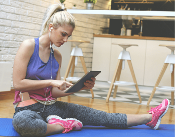 Young woman sitting on yoga mat in looking at an iPad.