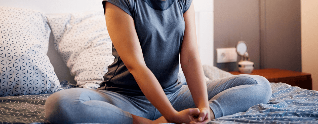 Young lady holding a yoga pose seated on her bed.