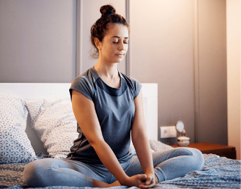 Young lady holding a yoga pose seated on her bed.