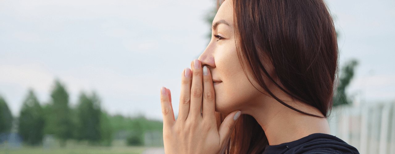 Side view of girl standing outside looking at sky with hands together as if praying.