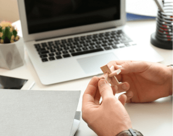 A closeup of hands holding wood puzzle pieces.