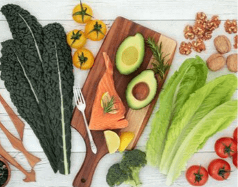 Top view of brain healthy foods like avocado, kale, tomatoes on a white wood background.