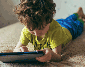 A young boy laying on top of his bed with a tablet.