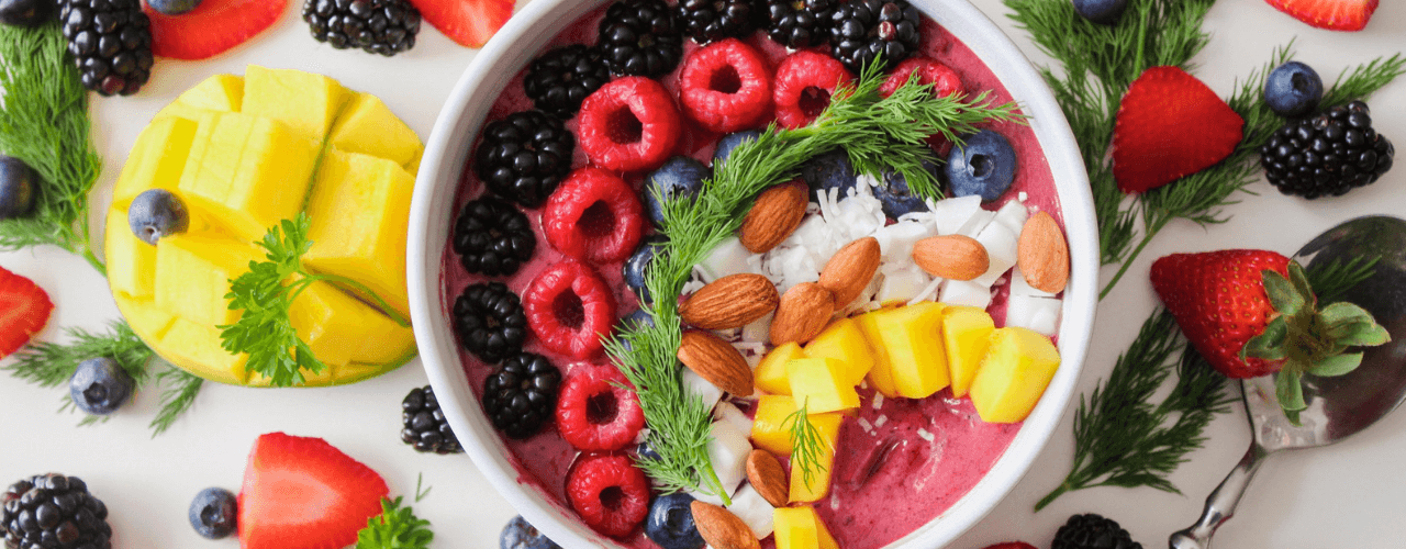 Top view of a bowl filled with black berries, raspberries, pineapple, blueberries, nuts and strawberries.