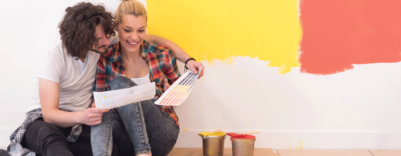 A couple sitting on the floor selecting paint swatches for a wall color.