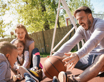 A mom, dad and 2 kids playing basketball outside.