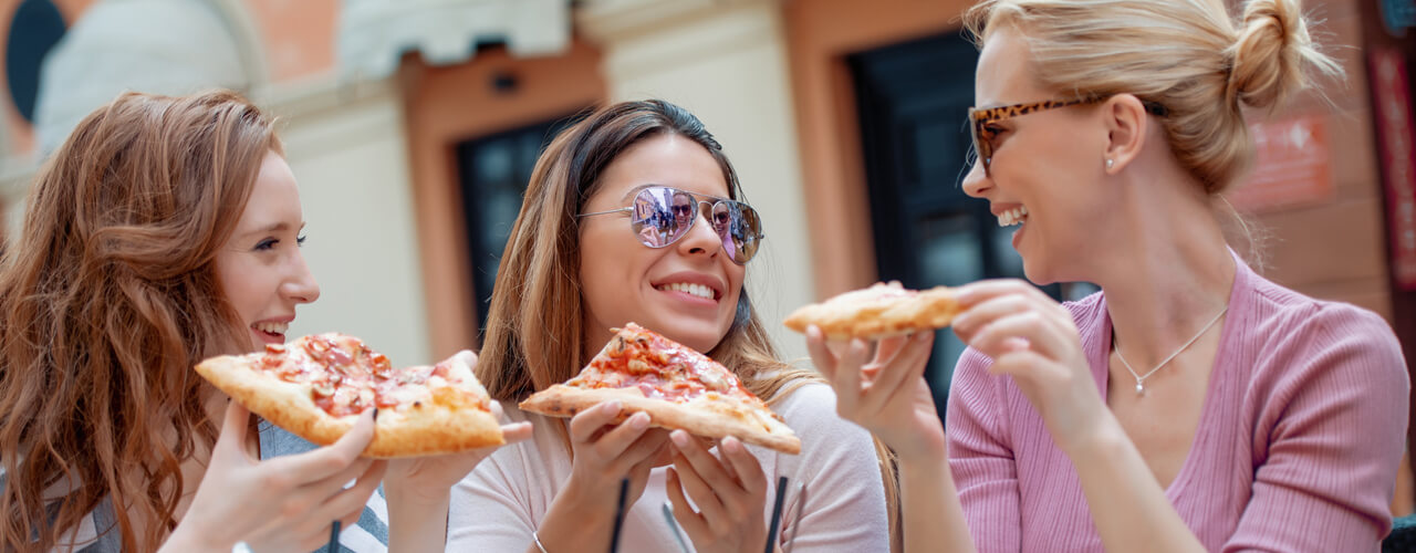 A group of friends seated at an outdoor patio laughing and eating pizza.