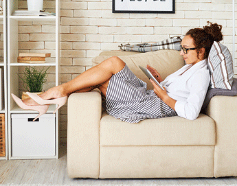 A girl laying across a living room chair with her legs up on the chair arm while looking at an iPad.