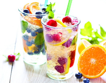 Two glasses with straws filled with crushed ice, lemons, limes, blueberries and raspberries.