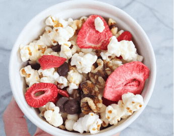 Top view of a bowl filled with nuts, berries and popcorn.