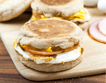 An egg and ham breakfast sandwich sitting on a cutting board.