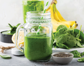 A St. Patrick's Day green smoothie in a glass next to bananas and kale.