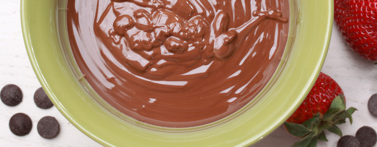 Chocolate pudding in a bowl next to chocolate morsels and strawberries.