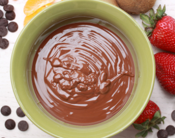 Chocolate pudding in a bowl next to chocolate morsels and strawberries.