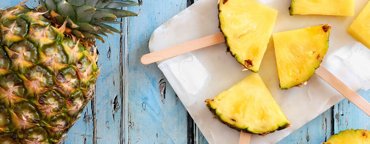 Pineapple sliced into small quarters with popsicle sticks pushed into the bottoms.