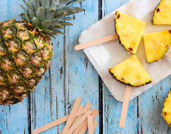 Pineapple sliced into small quarters with popsicle sticks pushed into the bottoms.