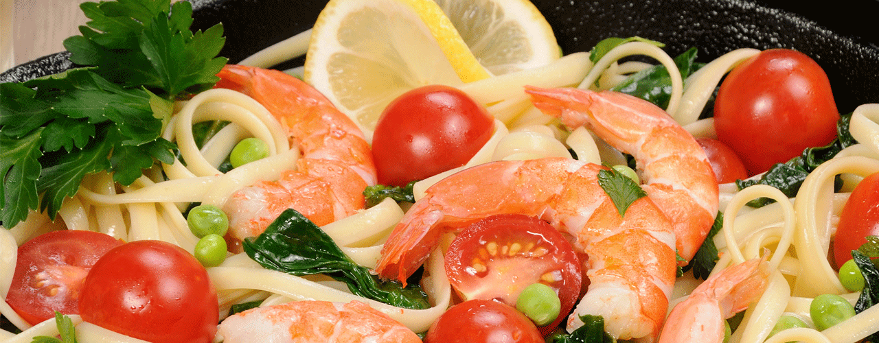 A bowl of pasta mixed with tomatoes, peas and shrimp.