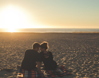 A couple snuggling on the beach watching the sunset.