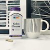 A bottle of 21st Colon Cleanse vegetarian capsules next to a coffee cup on a counter with abstract artwork in the background.