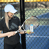 A woman at a tennis court holding a tennis rack, a tennis ball and a bottle of 21st Century Calcium 1200 mg Plus D3 10 mcg liquid filled, rapid release softgels.