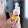 An older woman holding a bottle of 21st Century Estro Support Max Plus Energy tablets.