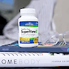 A bottle of 21st Century Health Eyes SuperView2 softgels on a stack of books with reading glasses on the right.